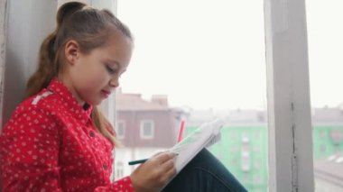 Pencere kenarında oturan ve çizim bir kız. Yakın çekim