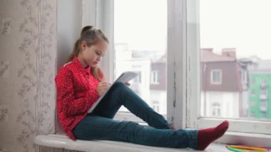 Pencere kenarında oturan ve çizim kırmızı gömlekli bir kız