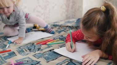 İki küçük kız yatakta yatıyordu ve bir şey ile renkli kalemler çizim. Yakın çekim