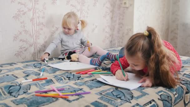 Две маленькие девочки лежат на кровати и рисуют что-то цветными карандашами. — стоковое видео