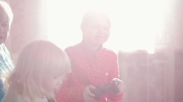 Uma avó a pentear o cabelo das netas. Outra menina jogando jogo com joystick — Vídeo de Stock