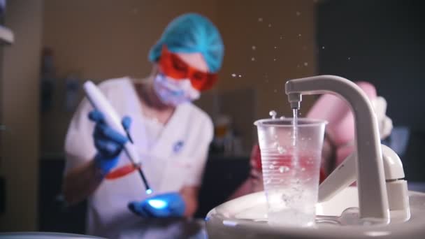 Odontologia, medicina. Dentista a trabalhar com a lâmpada. Água derramando no copo de plástico. Movimento lento — Vídeo de Stock