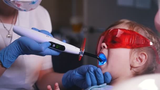 Odontología, medicina. Bebé en la recepción del dentista. Dentista trabajando con la luz de curado dental — Vídeos de Stock