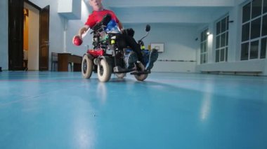 Engelli biri tekerlekli sandalyede. Kırmızı küçük topu atma. Büyük salon. Ağır çekim