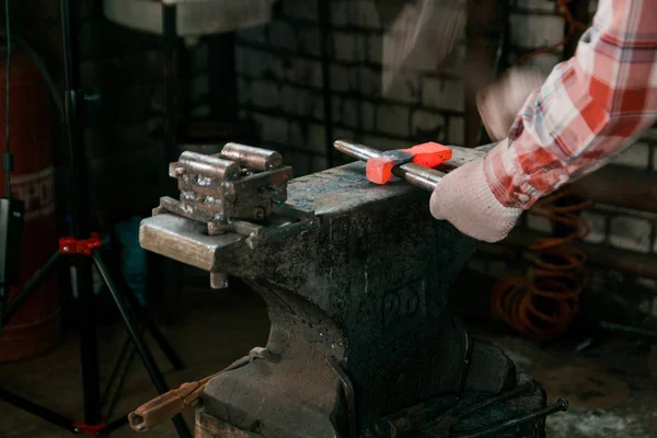 Ferreiro trabalhando com peça de metal quente vermelho de novo machado na bigorna na forja. Foco na bigorna — Fotografia de Stock