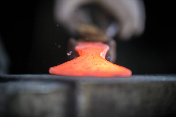 Кузнец и наковальня. Кузнец работает с красным горячим металлом заготовки нового молотка на наковальне в кузнице
