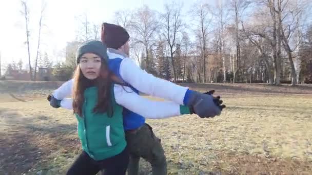 Un hombre joven y una mujer se están calentando en el parque de finales de otoño. Haciendo sentadillas al aire libre espalda con espalda . — Vídeo de stock