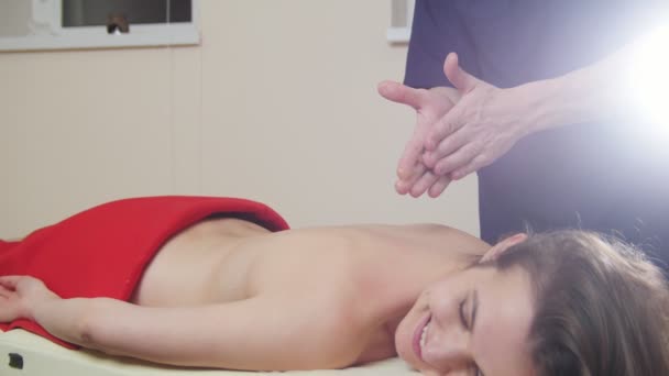 Sesión de masaje. Mujer joven se acuesta en el sofá y recibe un masaje relajante. Masajista frota el aceite entre tus manos — Vídeo de stock