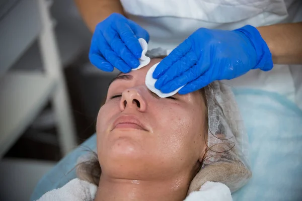 Klinik Kosmetologi. Seorang klien mengambil prosedur. Menyeka wajah klien . — Stok Foto