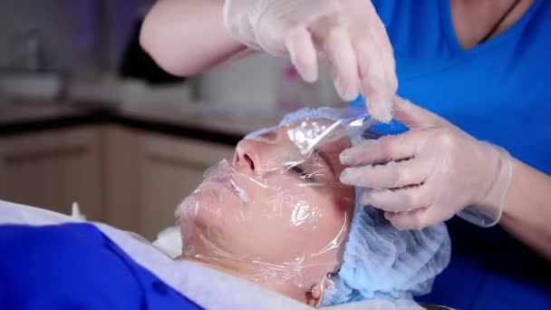 Sesión de masaje. Una mujer recibiendo un masaje facial. Preparando la cara. Pelar el polietileno — Vídeo de stock