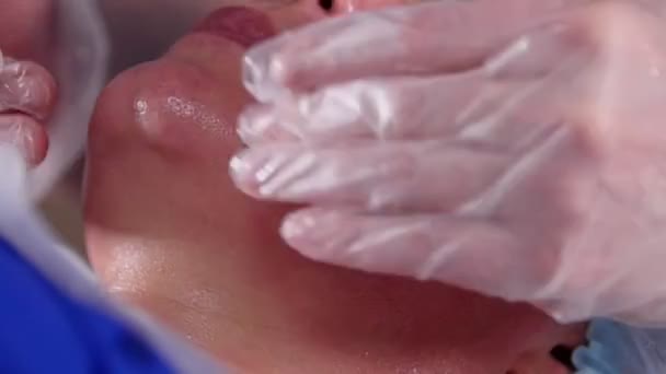 Clínica de beleza. Jovem mulher recebe massagem facial relaxante com creme por massagista profissional em máscara . — Vídeo de Stock