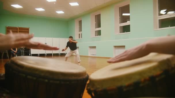 Μαχητής εκτελεί πολεμικές κόλπα με στοιχεία χορού στο παρασκήνιο παίζει ένα δύο jembe μουσικά όργανα — Αρχείο Βίντεο