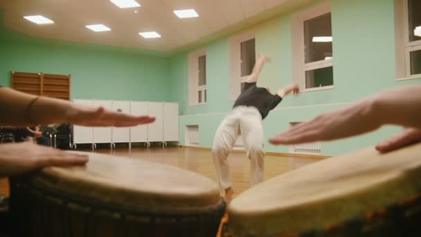 Винищувач виконує бойові трюки на фоні, граючи на двох музичних інструментах джембе або атабаке — стокове відео
