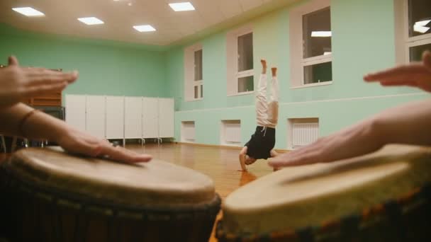Vechter uitvoert martial trucs op de achtergrond spelen een atabaque twee muziekinstrumenten — Stockvideo