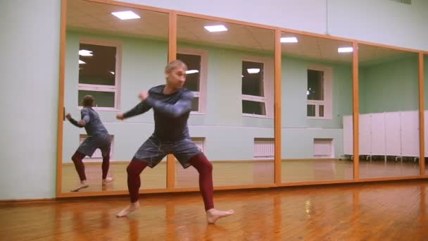 Muž bojovník provádí bojové triky s taneční prvky v tělocvičně sportovní před zrcadlem — Stock video