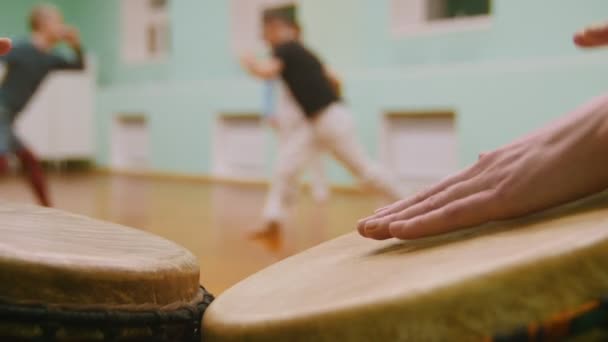 Tocar dos instrumentos musicales jembe o atabaque en el fondo de combate masculino realiza trucos marciales en el gimnasio deportivo — Vídeo de stock