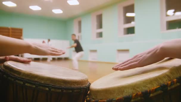 Combattant effectue des tours martiaux avec des éléments de danse sur fond jouant un jembé deux instruments de musique ou atabaque — Video