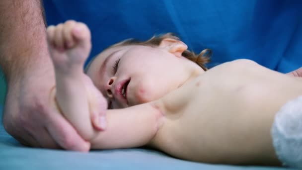 Medical centre. A little baby with cerebral palsy disorder lays on a medical couch while doctor doing exercises on their legs — Stock Video