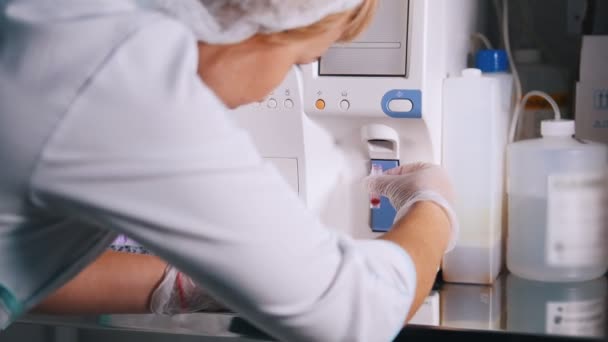 Medische kliniek. Verpleegkundige neemt het bloedmonster uit de machine en wacht op de resultaten — Stockvideo