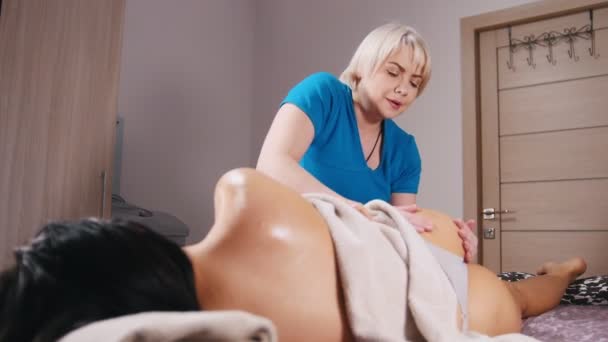 Sessão de massagem. Uma mulher deitada no sofá ao seu lado e conversando com uma massagista enquanto recebe uma massagem — Vídeo de Stock