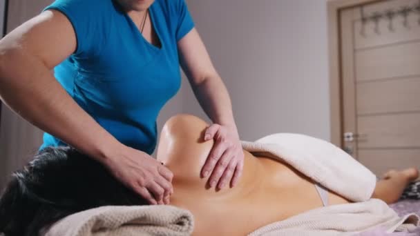 Sessione di massaggi. Una donna sdraiata sul divano sul fianco e che riceve un massaggio. Massaggiare i muscoli della schiena — Video Stock