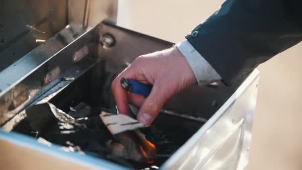有门廊的烤架。一个男人用烧焦的纸点燃烤架上的煤 — 图库视频影像