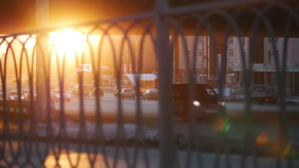 Autos, die bei Sonnenuntergang auf der Straße fahren. ein Blick durch einen unkonzentrierten Zaun im Vordergrund — Stockvideo
