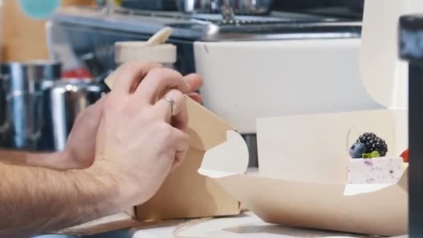 Uma padaria. Um homem embalando um pequeno bolo na caixa de papelão — Vídeo de Stock