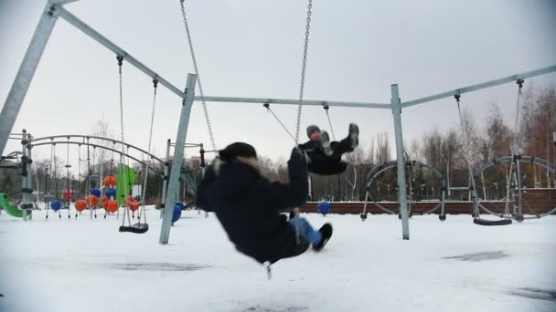 Two young kids having fun on the playground. Swinging in slow motion. Winter — Stock Video