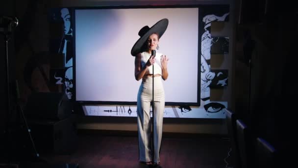 Una mujer con un gran sombrero retro de pie en el escenario y cantando con un micrófono — Vídeos de Stock