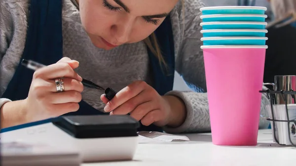 En kvinna barista skriva något på papper. Färgstarka koppar på förgrunden. — Stockfoto