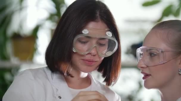 Chemielabor. zwei junge Frauen halten eine Flasche mit rosa Flüssigkeit in der Hand — Stockvideo