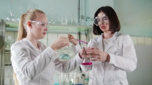 Химическая лаборатория. Два молодых лаборанта проводят эксперименты с жидкостями — стоковое видео