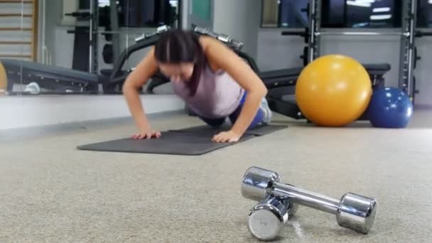 A képzés. Egy fiatal nő során push ups. Az előtérben a súlyzók — Stock videók