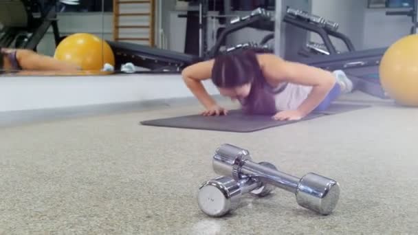 A treinar. Uma jovem a fazer flexões no ginásio. halteres em primeiro plano — Vídeo de Stock