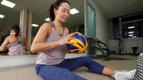 Entrenamiento. Una joven sentada en el suelo entrena sus manos con una pelota. Gimnasio — Vídeos de Stock