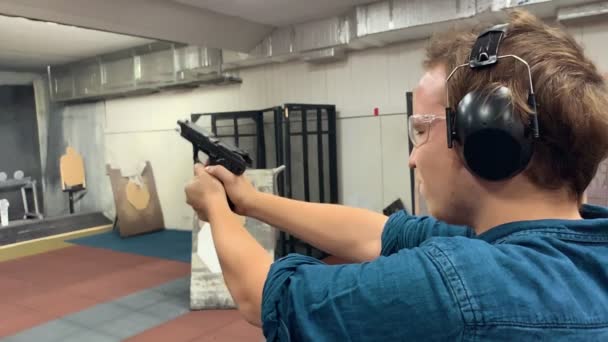 Jovem aponta, segurando uma arma em uma galeria de tiro, tiro alcance. Movimento lento — Vídeo de Stock