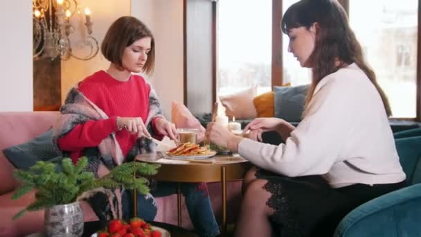 Две молодые женщины сидят в кафе и разговаривают во время поедания блинов — стоковое видео