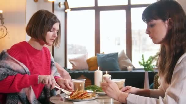 Két fiatal nő ül a kávézóban és palacsintát evés közben beszélt. Nagy modern belső — Stock videók
