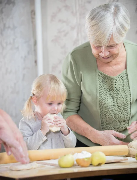 Старушка делает пирожки со своей внучкой. Девушка пробует тесто — стоковое фото