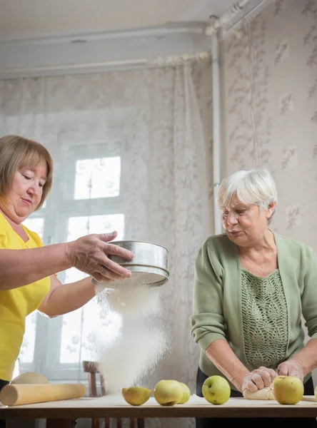 Two old women are making little pies. Sifting the flour