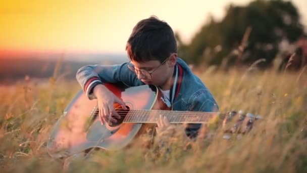 Kisfiú, kerek szemüveg játszik gitáron — Stock videók