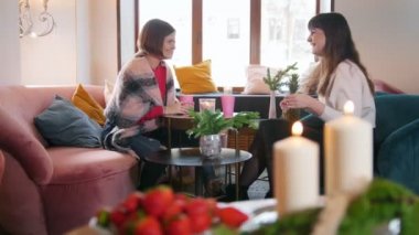 Kafede otururken, konuşurken ve kahve yudumlarken gülüyor iki genç kadın.