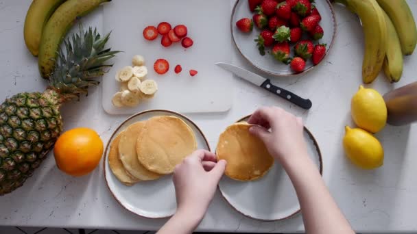 Een vrouw legt bananen op pannenkoeken en giet de gecondenseerde melk — Stockvideo