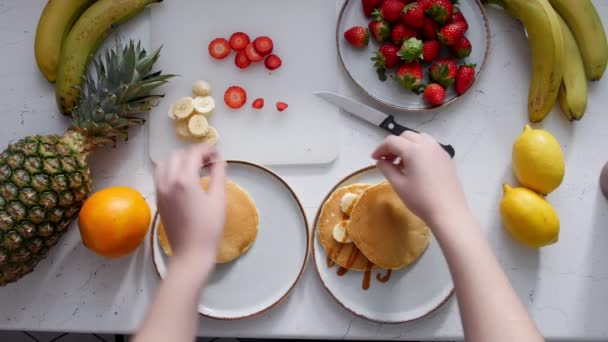 En kvinna lägger jordgubb på pannkakor och häller kondenserad mjölk — Stockvideo