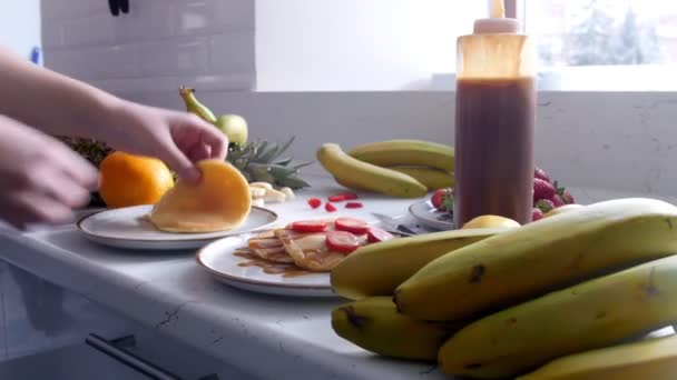 Küche - eine Frau legt Bananen auf Pfannkuchen und gießt Kondensmilch ein — Stockvideo