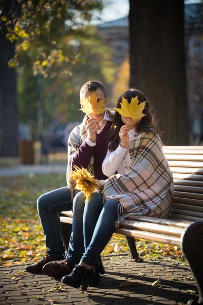 Milující pár sezení a kryt, obličej s podzimní listy v parku — Stock fotografie