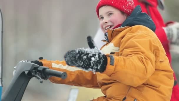 Χαμογελαστό αγόρι κάθεται σε ένα snowmobile και καλώντας σε αυτόν μέσα στο δάσος του χειμώνα — Αρχείο Βίντεο