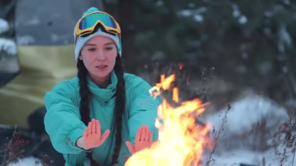 Flickan värmer händerna över brasan i skogen — Stockvideo