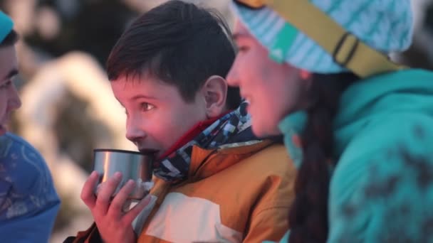 The child drinks tea near the fire, and adults tell him a story — Stock Video
